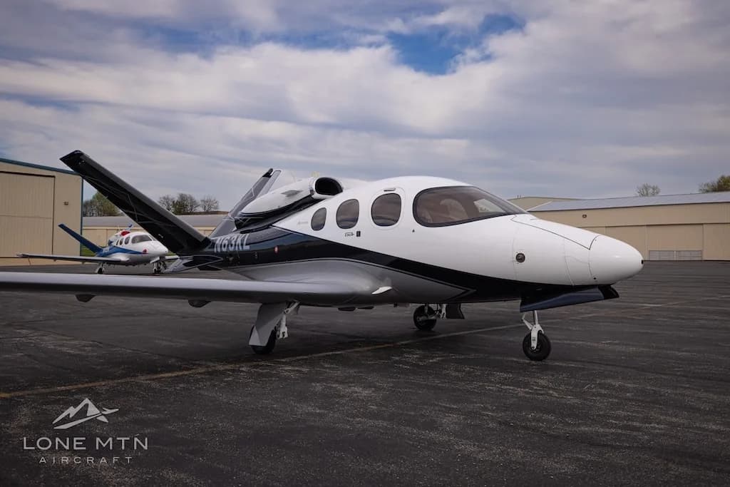 A white and black Cirrus Vision Jet (N63KL) parked on an asphalt apron with hangars in the background.