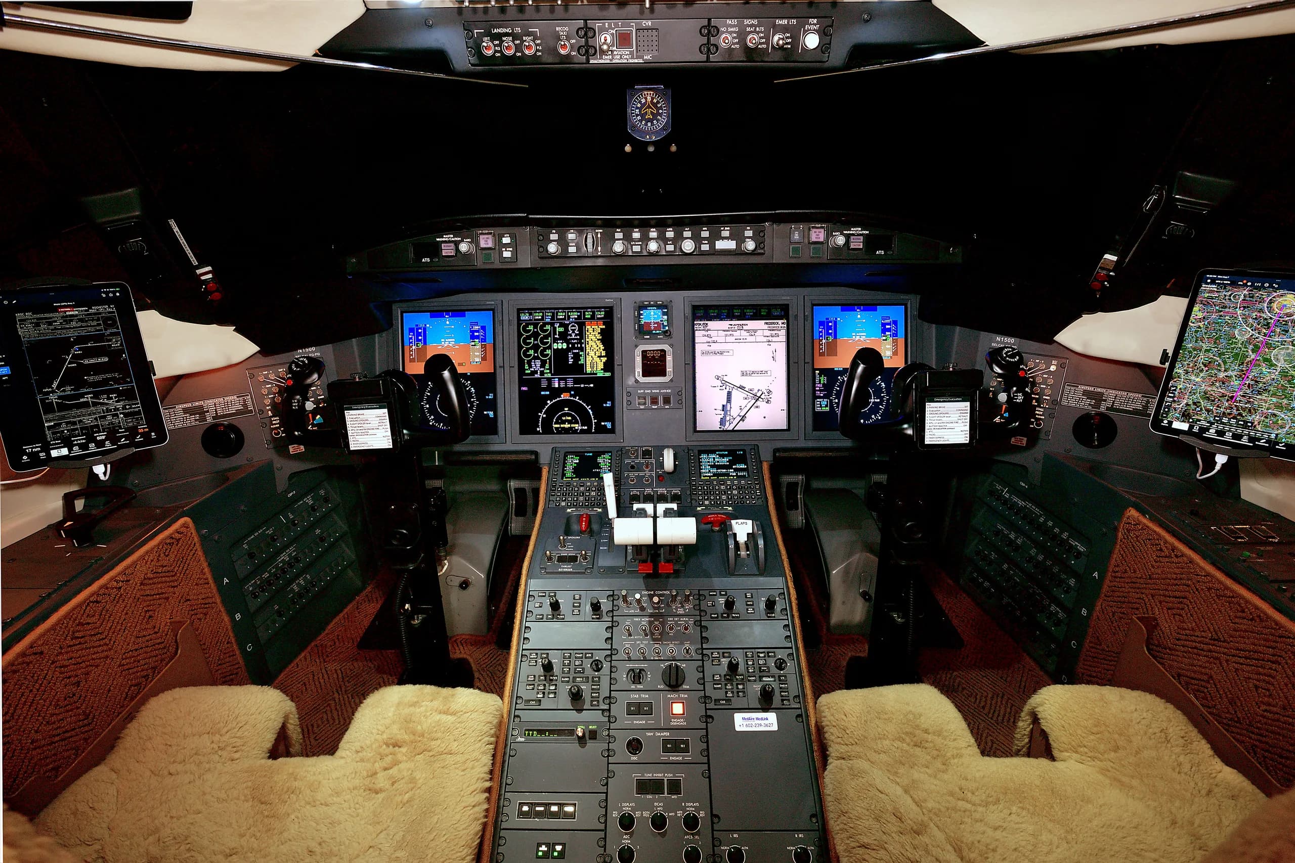 The modern cockpit of a private jet with multiple digital displays, control yokes, and a central throttle quadrant.