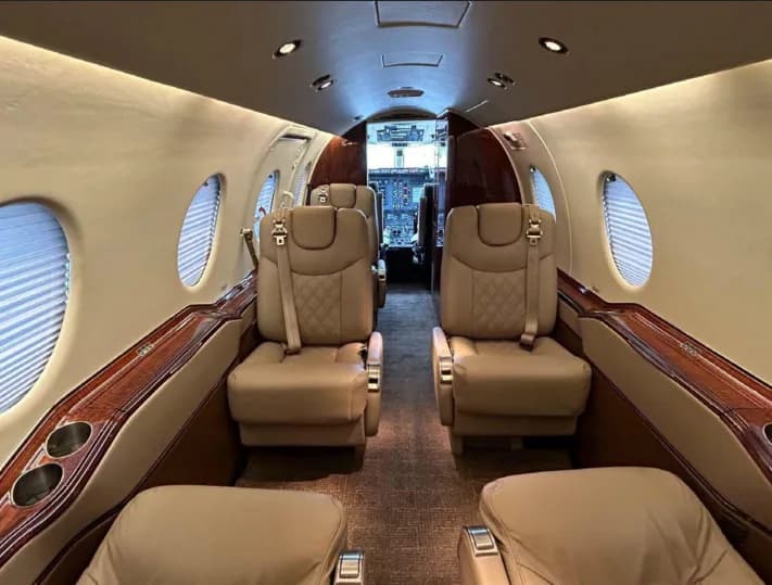 Aircraft cabin with tan leather seats, wood trim, and view towards the cockpit.