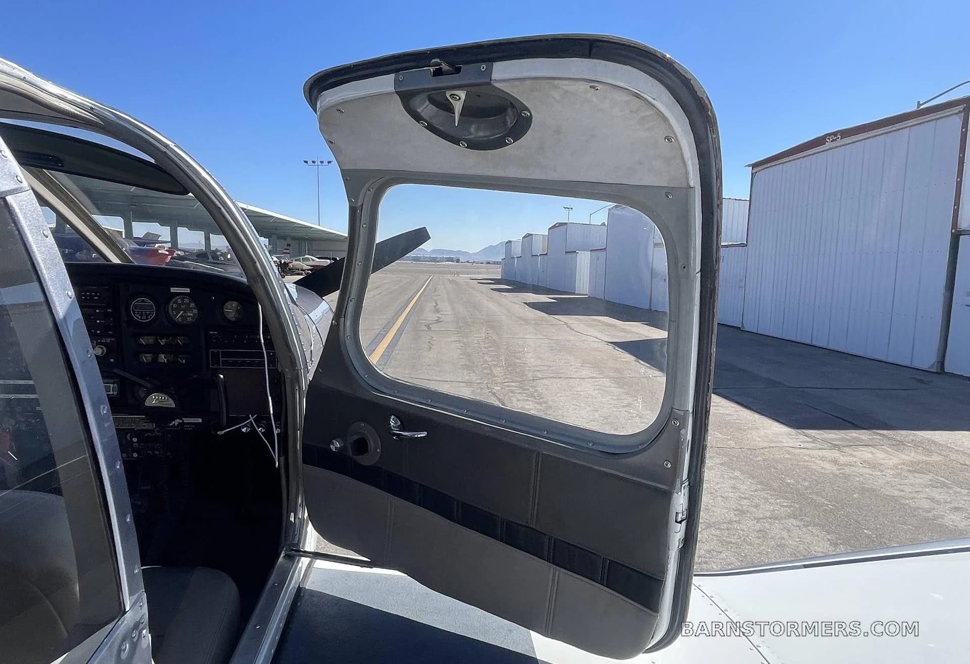 View from inside a Piper Cherokee 140 cockpit looking out through an open door onto an airfield runway.
