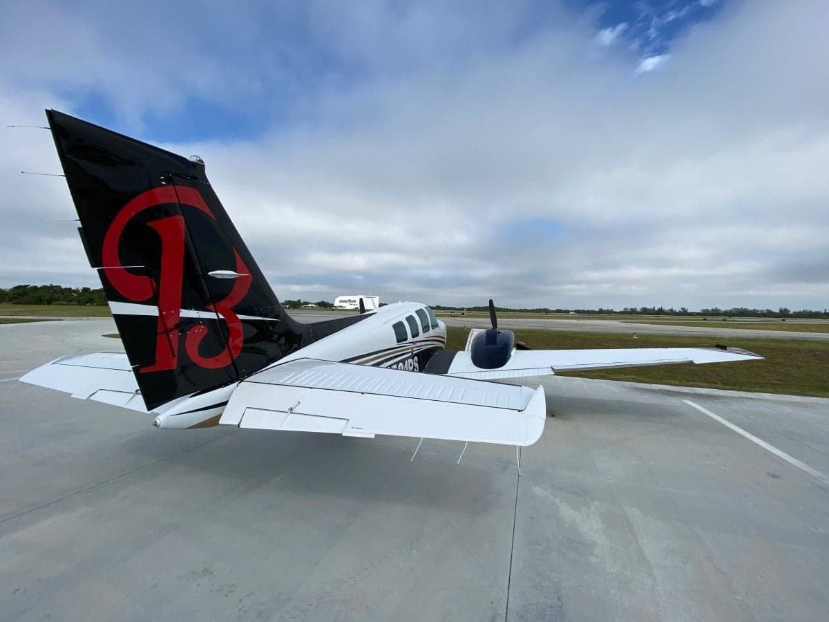 A rear view of a white and black twin-engine aircraft with registration N581PS, featuring a red 'B' logo on the tail, parked on an airfield.