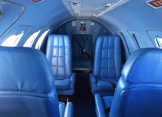 The aircraft cabin features blue leather seats arranged in a club configuration.