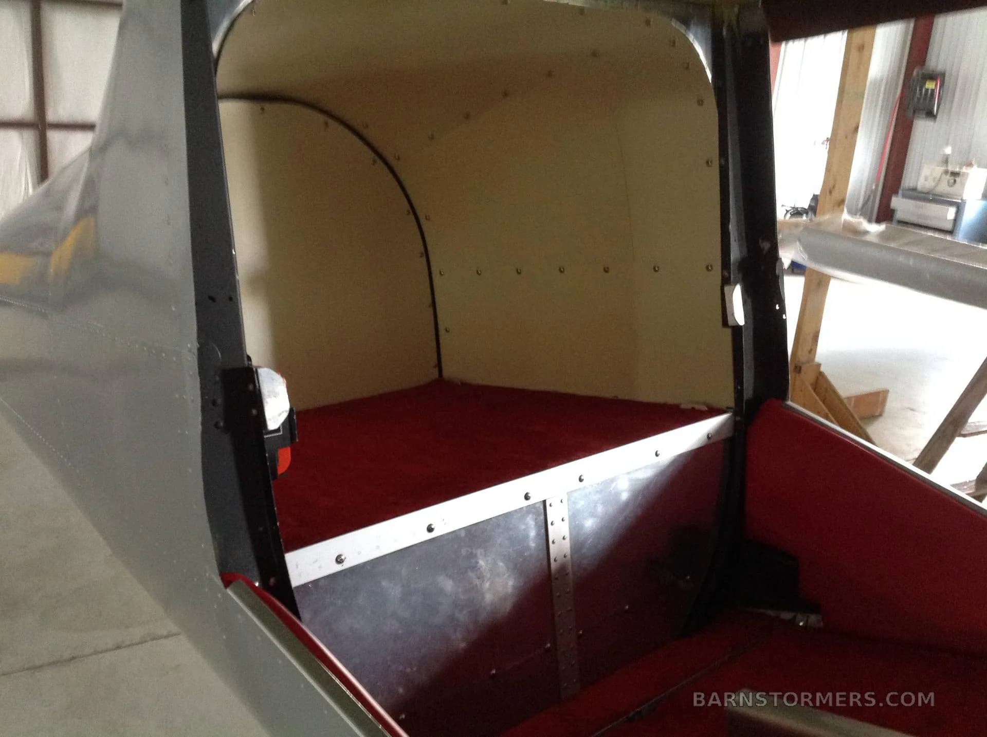 The rear cargo or passenger compartment of an aircraft, featuring red flooring and light-colored side panels.