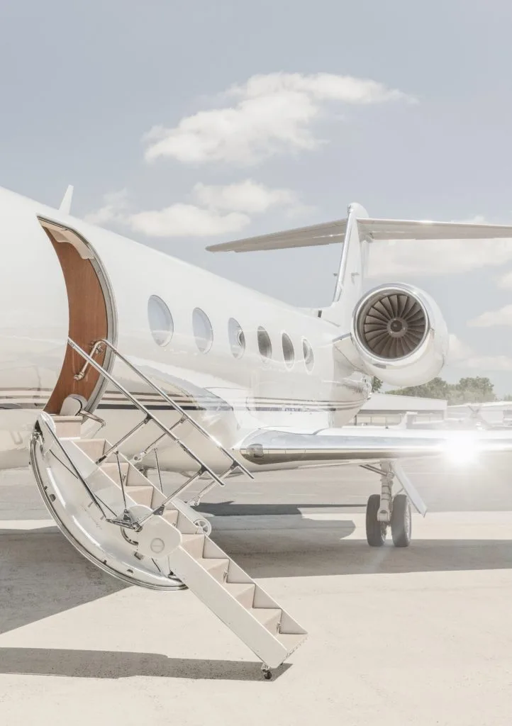 A white Gulfstream business jet parked on an airfield with its airstairs extended.
