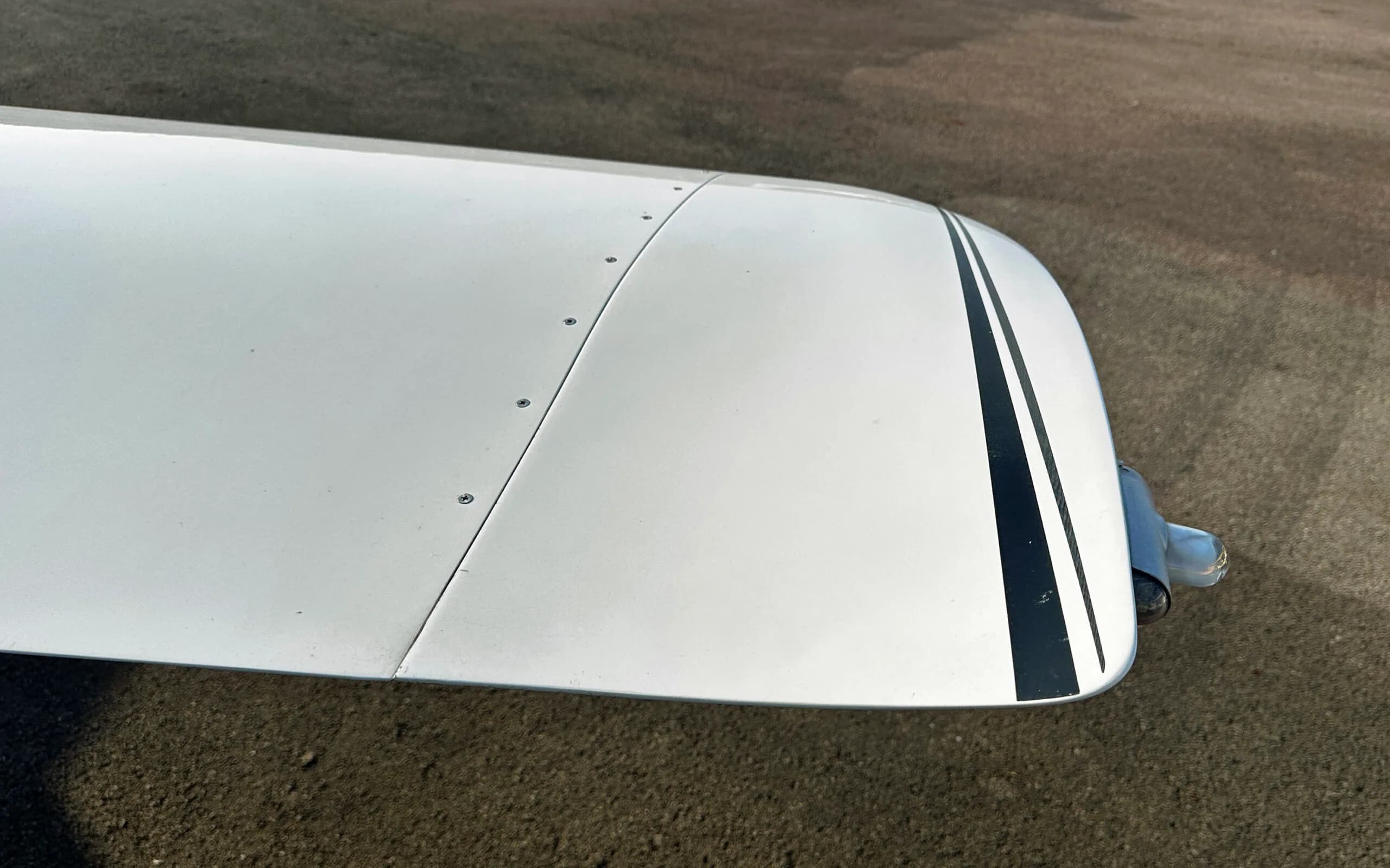 Top-down close-up view of the white wingtip of a Cirrus SR22 Turbo aircraft with black stripes.