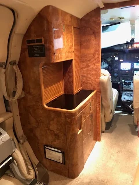 View of the Cessna Citation interior with wood accents and a refreshment center.