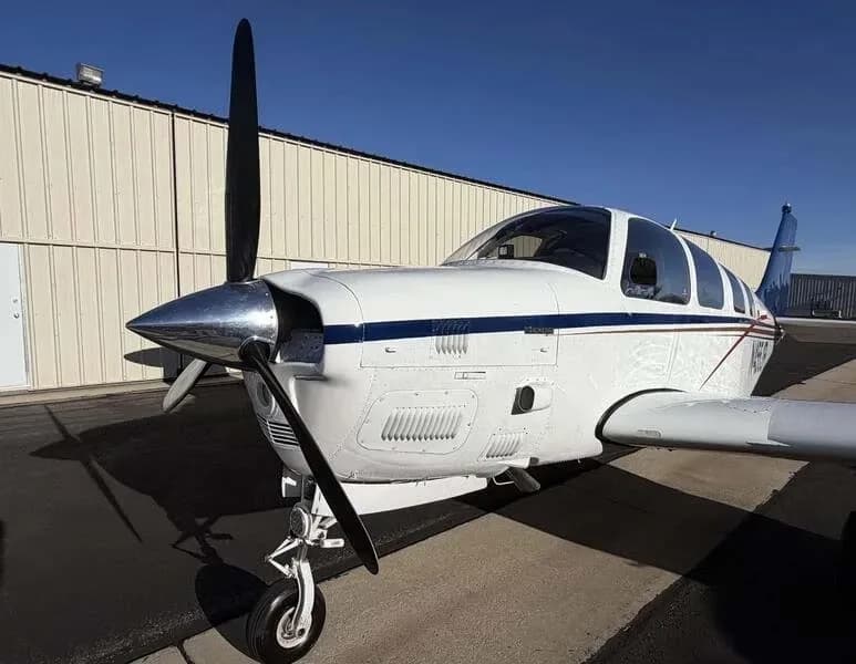 A front-quarter view of the white Beechcraft Bonanza N455JR showing its propeller and nose cone.