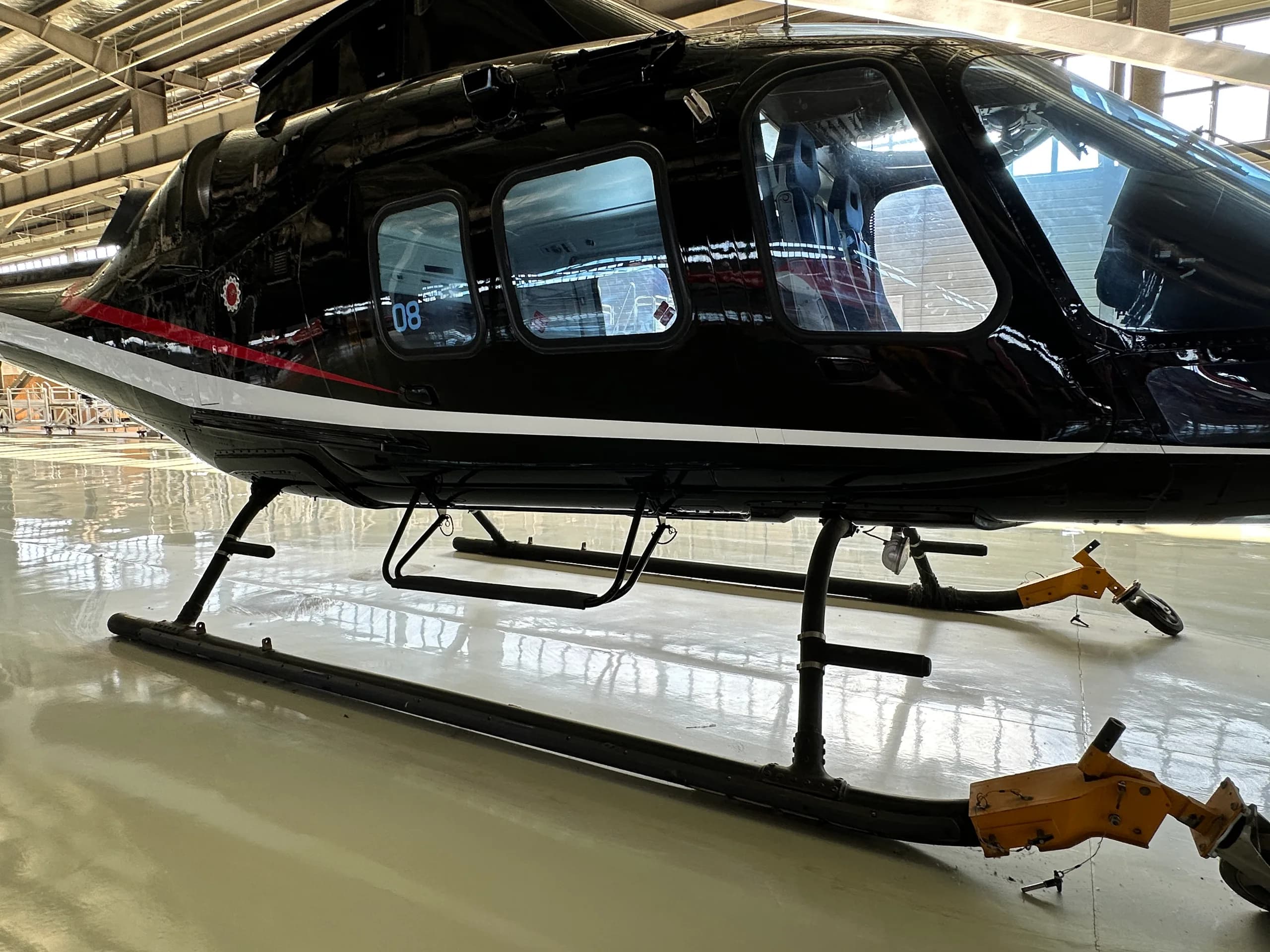 A close-up view of the black helicopter's fuselage with white and red stripes, showing the landing skids and passenger windows.