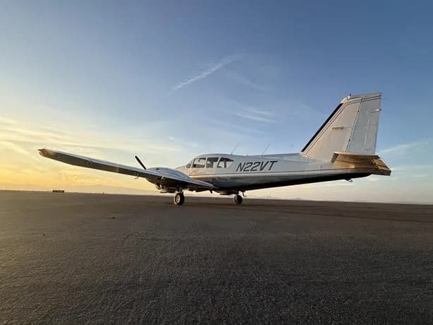 A rear-side view of a silver and black single-engine aircraft, N22VT, parked on an asphalt runway at sunset.