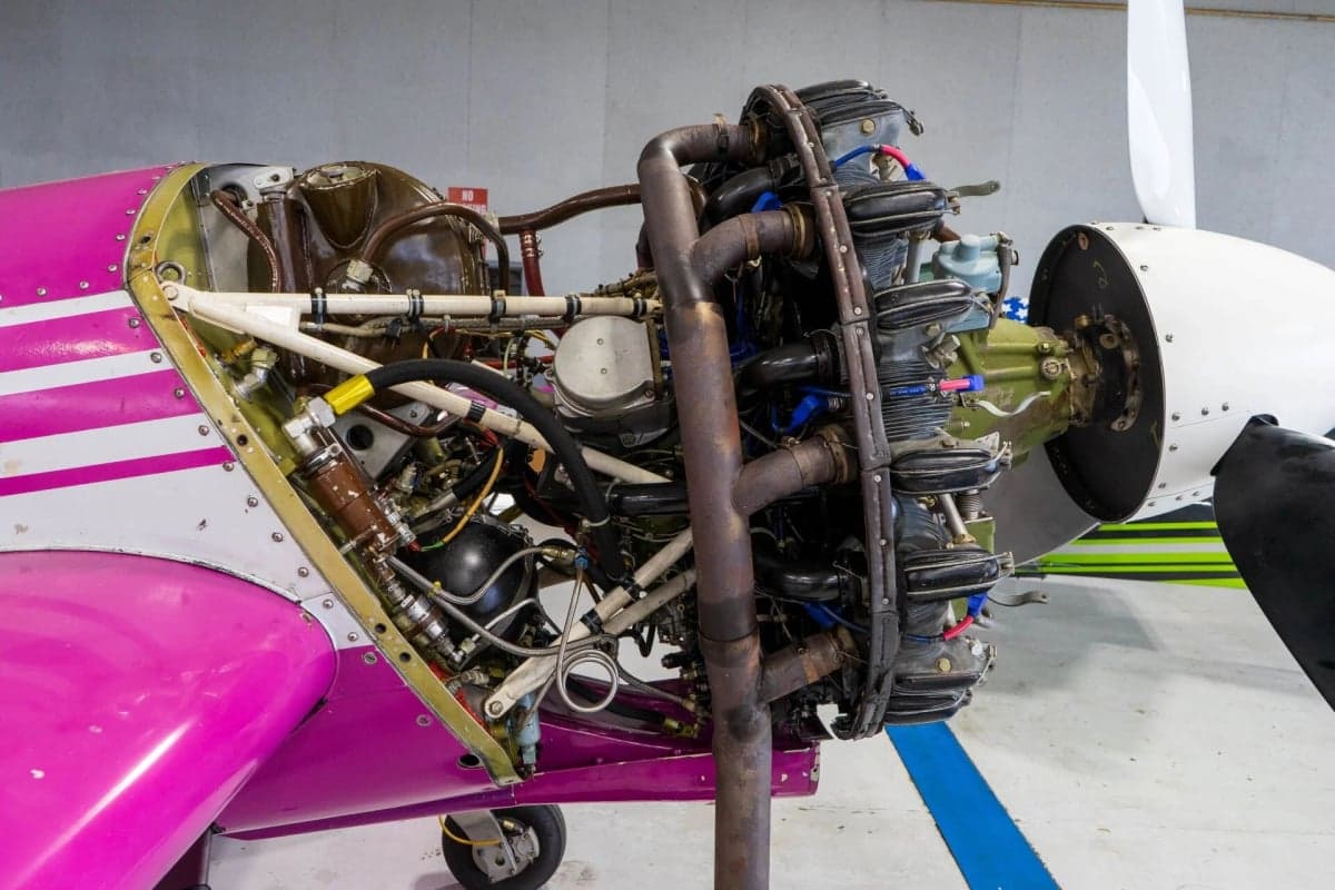 Close-up of the engine and propeller of a pink and white Sukhoi Su-26 aircraft.