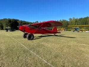 A red Cubcrafters aircraft is parked on a grassy field.