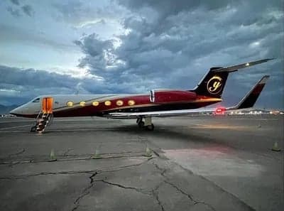 A Gulfstream G550 aircraft is parked on the tarmac with the stairs down, under a cloudy sky.