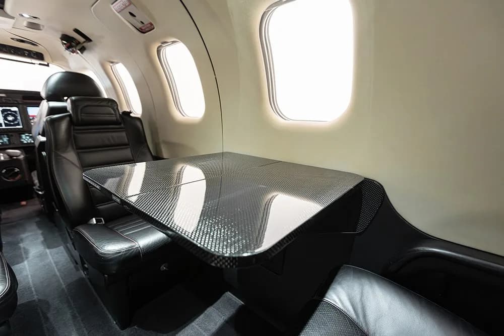 The luxurious interior cabin of the TBM 930 aircraft, featuring black leather seats and a carbon fiber table.