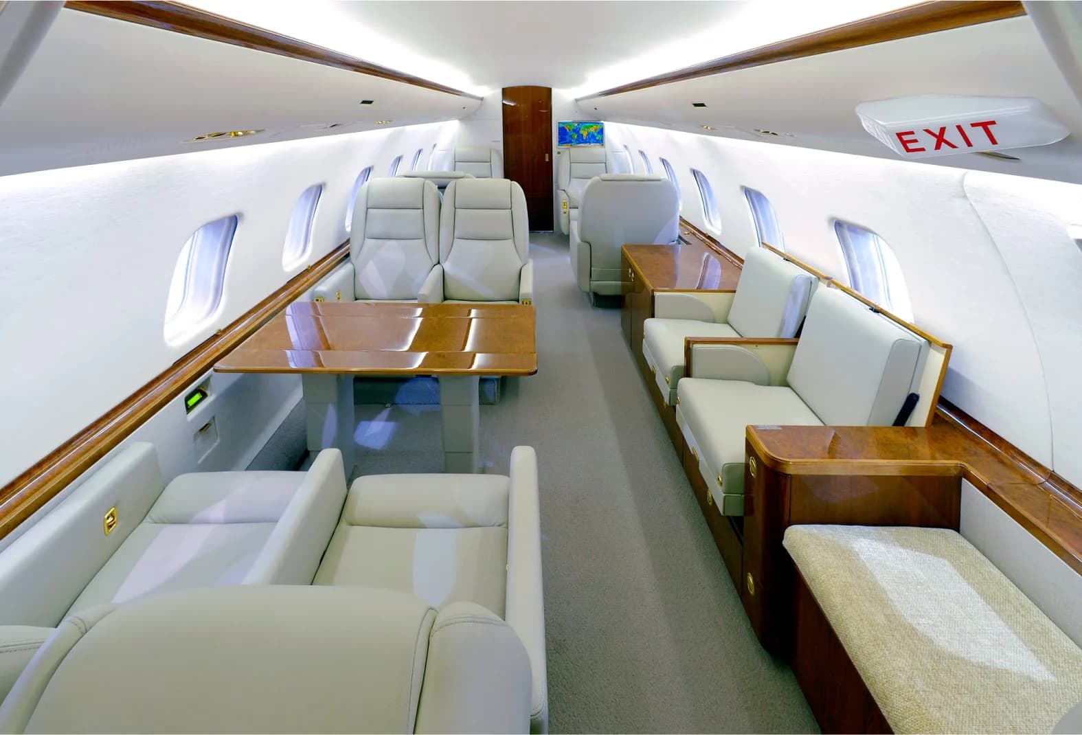 The luxurious interior cabin of a private jet with light-colored leather seats, wooden tables, and an 'EXIT' sign.