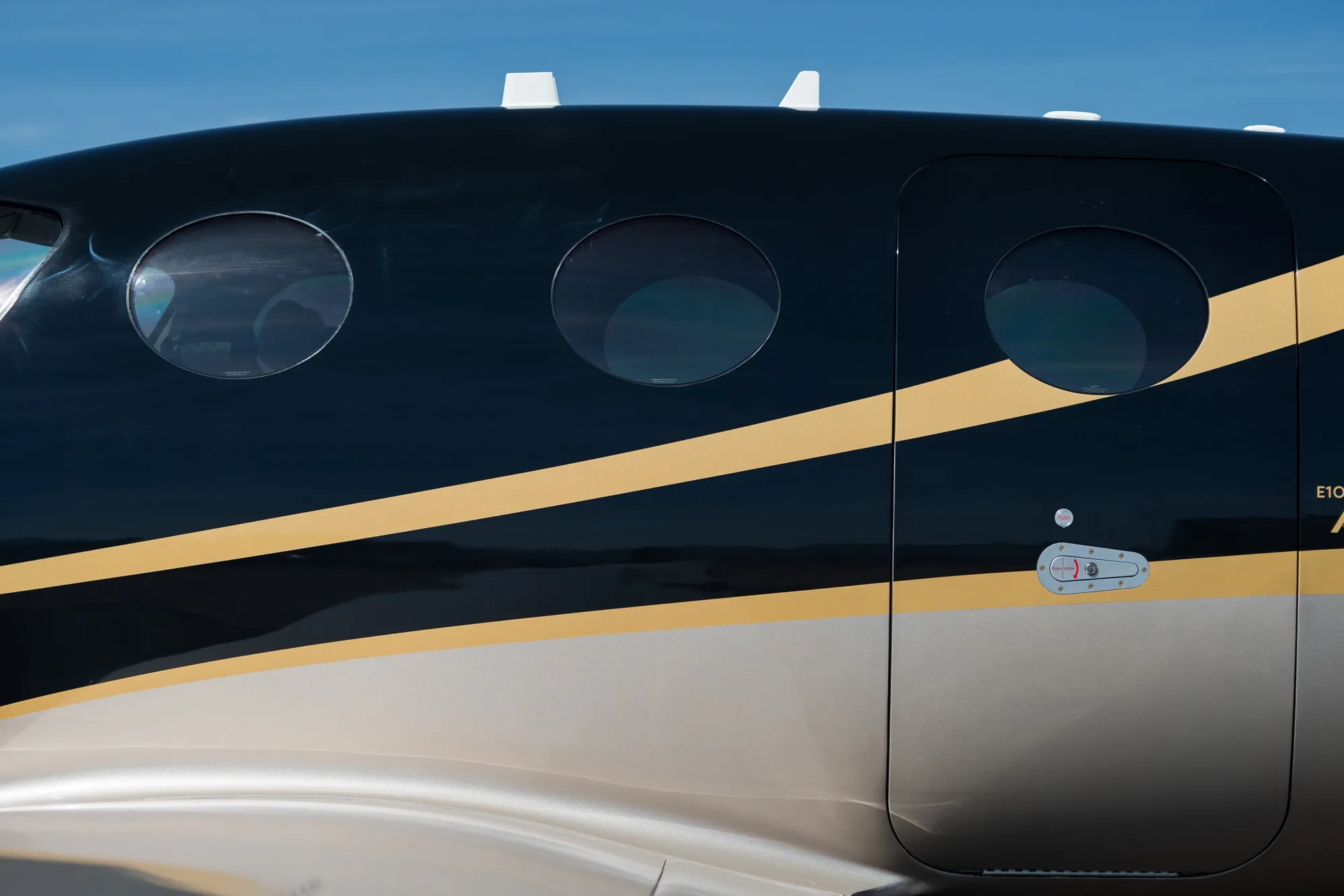 A close-up of the black and gold fuselage of the Epic E1000 GX aircraft, showing windows and the main cabin door.