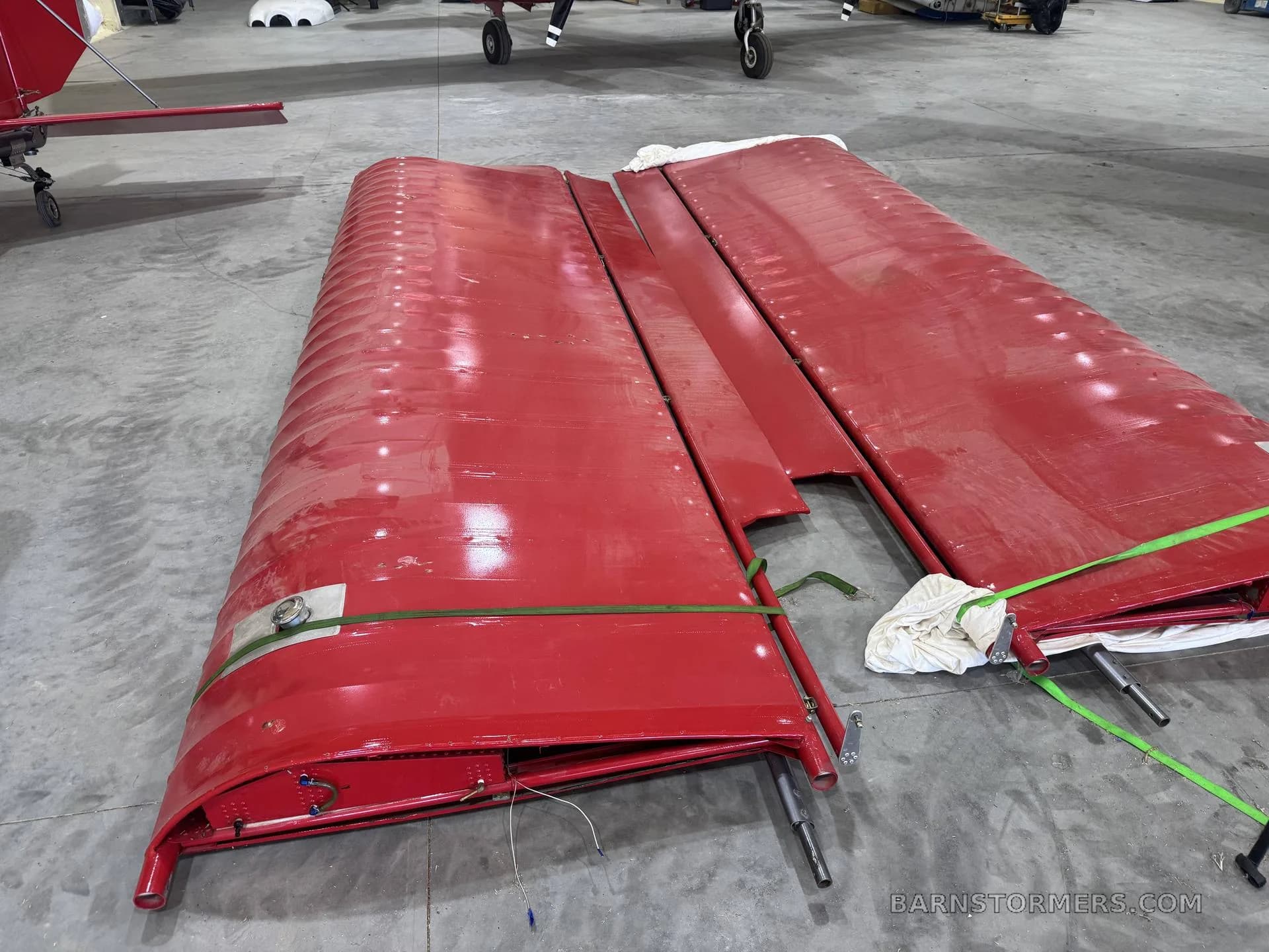 Two disassembled red aircraft wings, secured with green straps, lying on a concrete hangar floor.