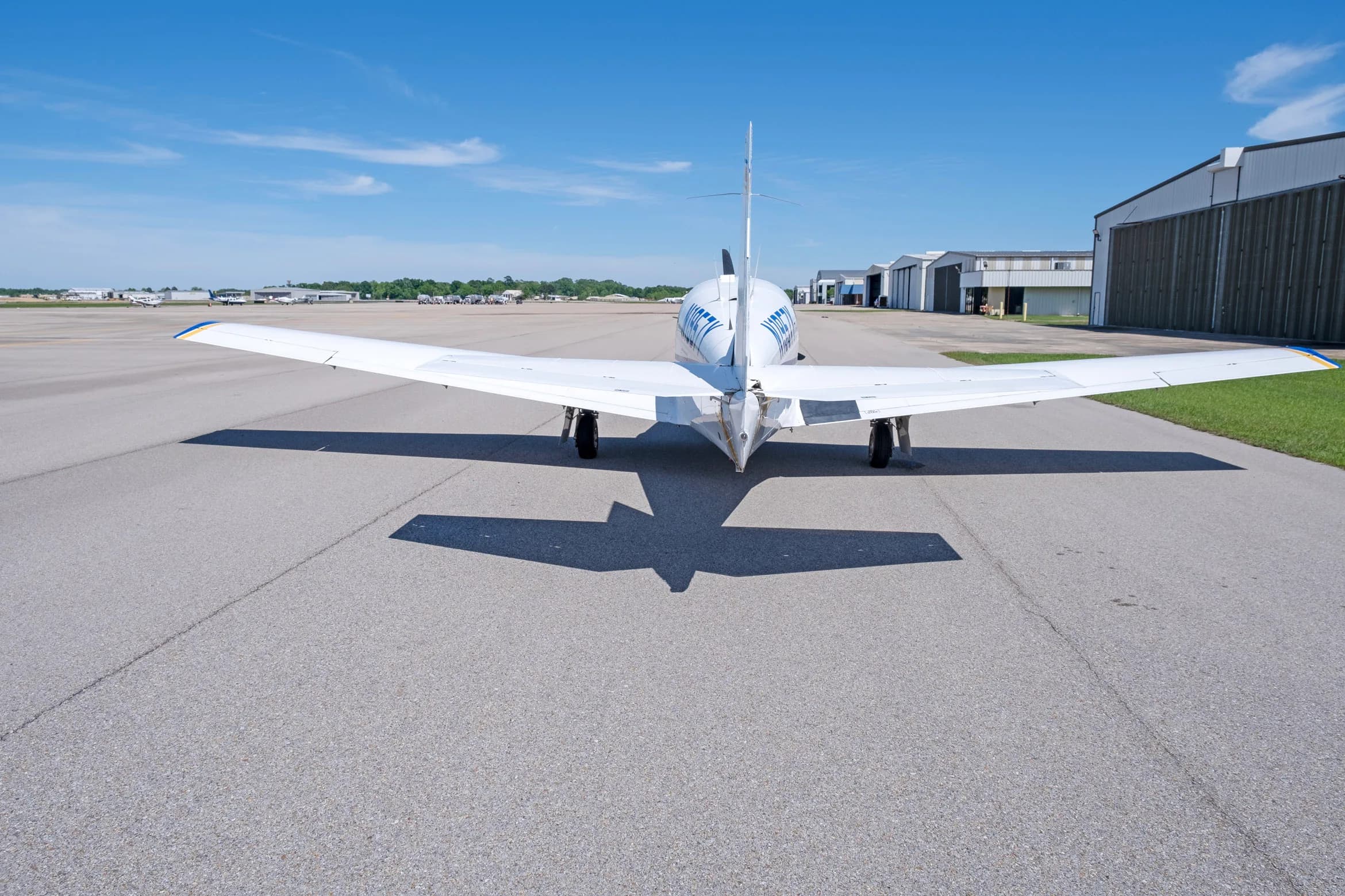A rear view of a white single-engine propeller aircraft with blue and yellow stripes, registration N1957Y, parked on an asphalt apron.