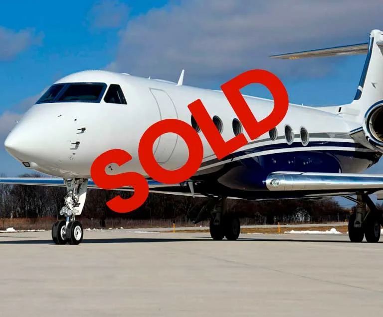 A white business jet with a blue stripe on the fuselage, parked on an airport tarmac under a blue sky, with a large red 'SOLD' overlay.
