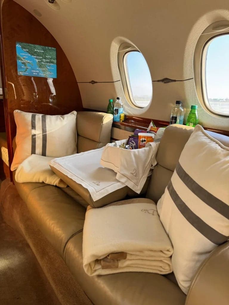 A view of the aircraft's interior with a tan leather seat, pillows, and a tray with snacks and drinks.