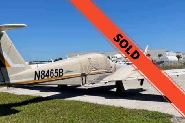 A cream-colored Piper Meridian aircraft with orange and white stripes, registration N8465B, parked on a tarmac.