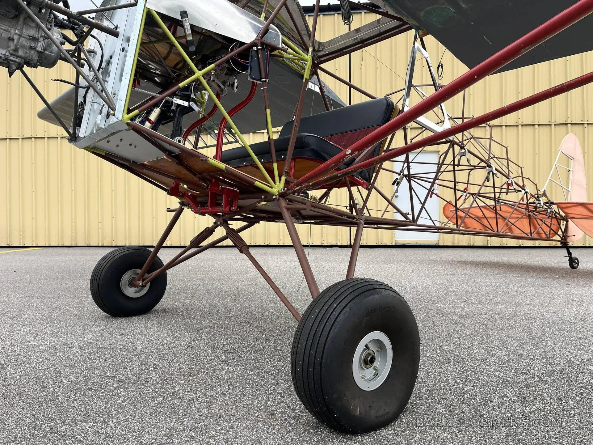 A low-angle view showing the main landing gear and the exposed tubular frame of an ultralight aircraft.