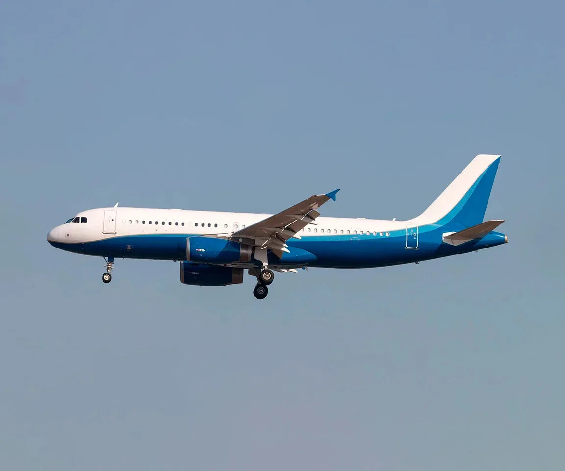 A white and blue Airbus A320 family aircraft in flight against a clear blue sky.