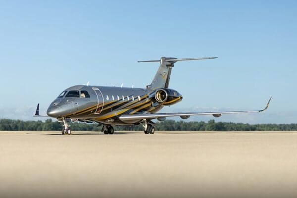 A silver and black Embraer Legacy 500 private jet with yellow stripes on a tarmac.