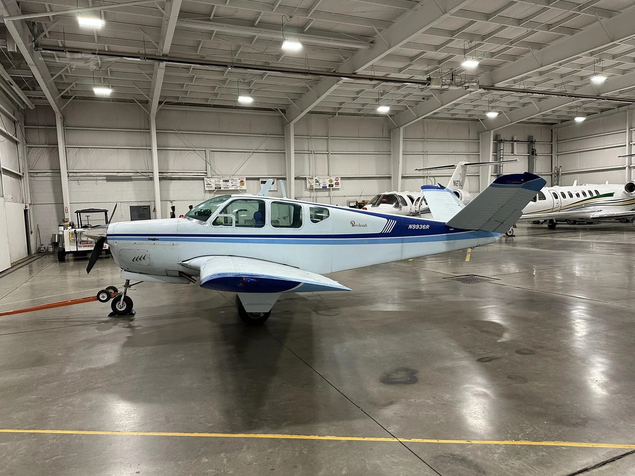 A white and blue Beechcraft Bonanza N9936R parked in a hangar, viewed from the front left.