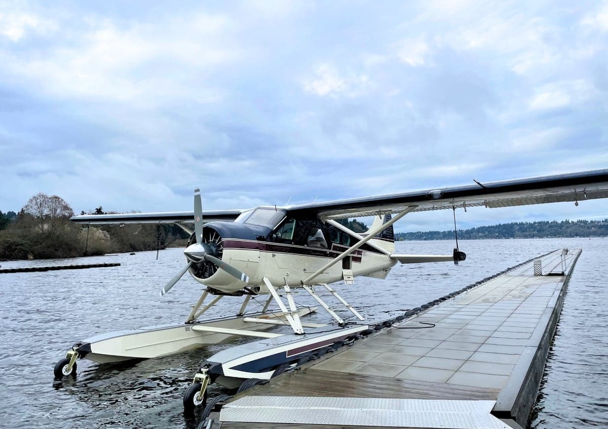 A white and maroon floatplane is docked at a pier on a cloudy day.