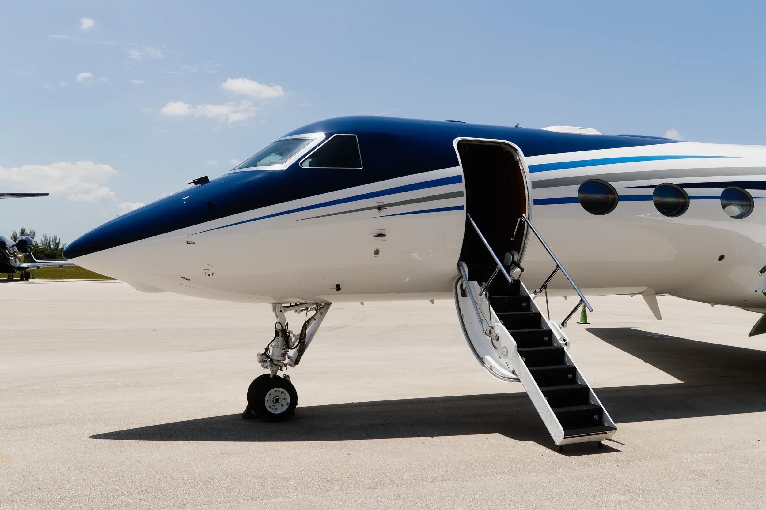 The front section of a blue and white Gulfstream G550 business jet with its passenger door and airstairs extended.