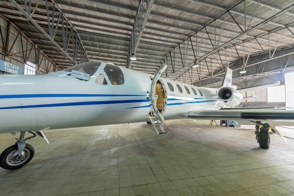 A white Cessna Citation II aircraft with blue stripes is parked in a hangar with its door open.