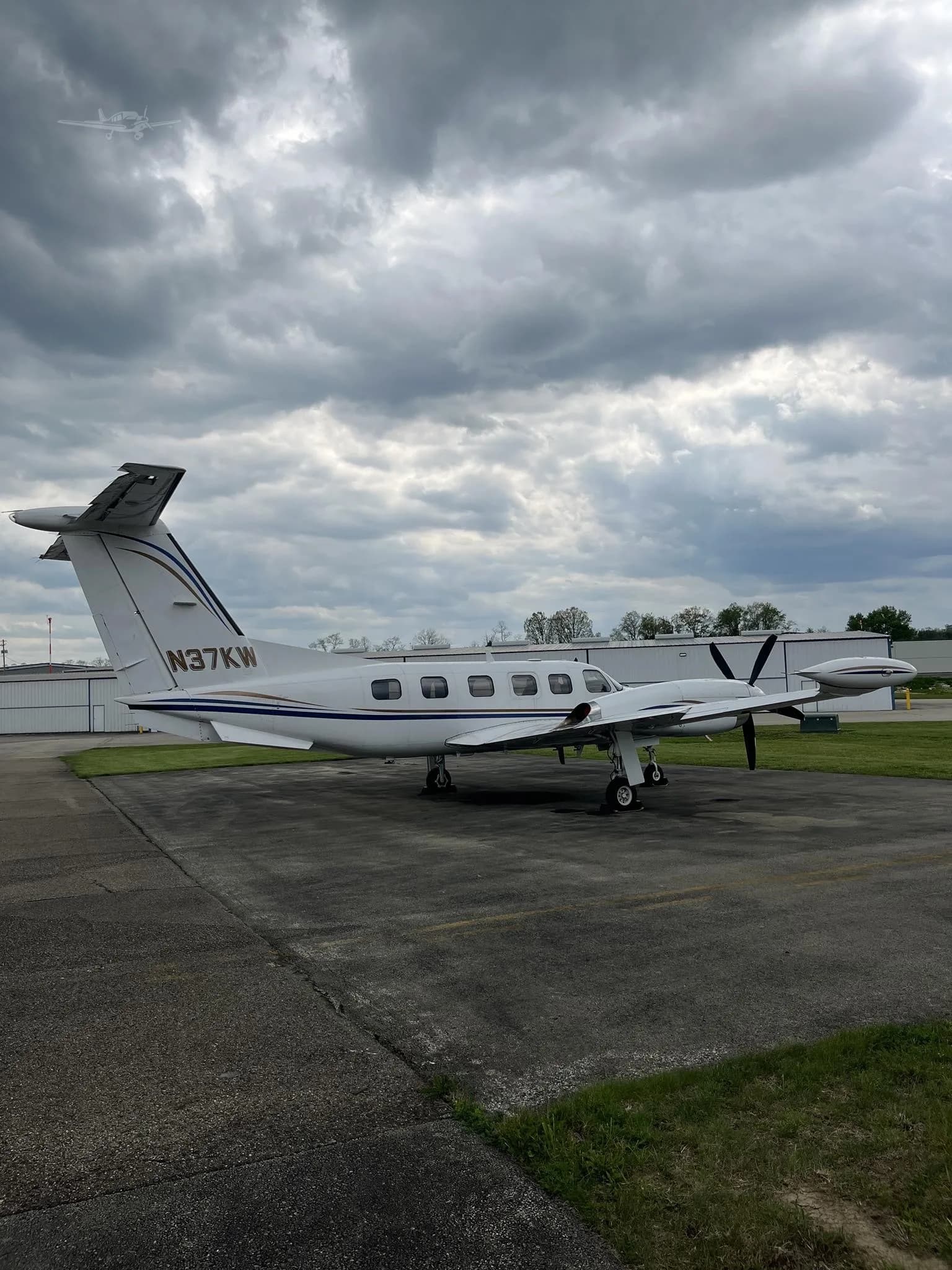 Side view of a white twin-engine turboprop aircraft (N37KW) with blue and gold stripes on the tail, parked on an airfield.