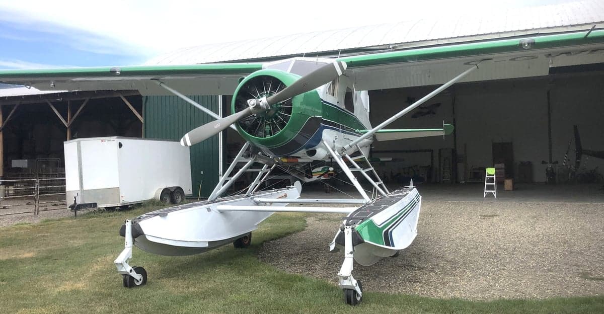 Front view of a green and white float plane parked in front of a hangar.