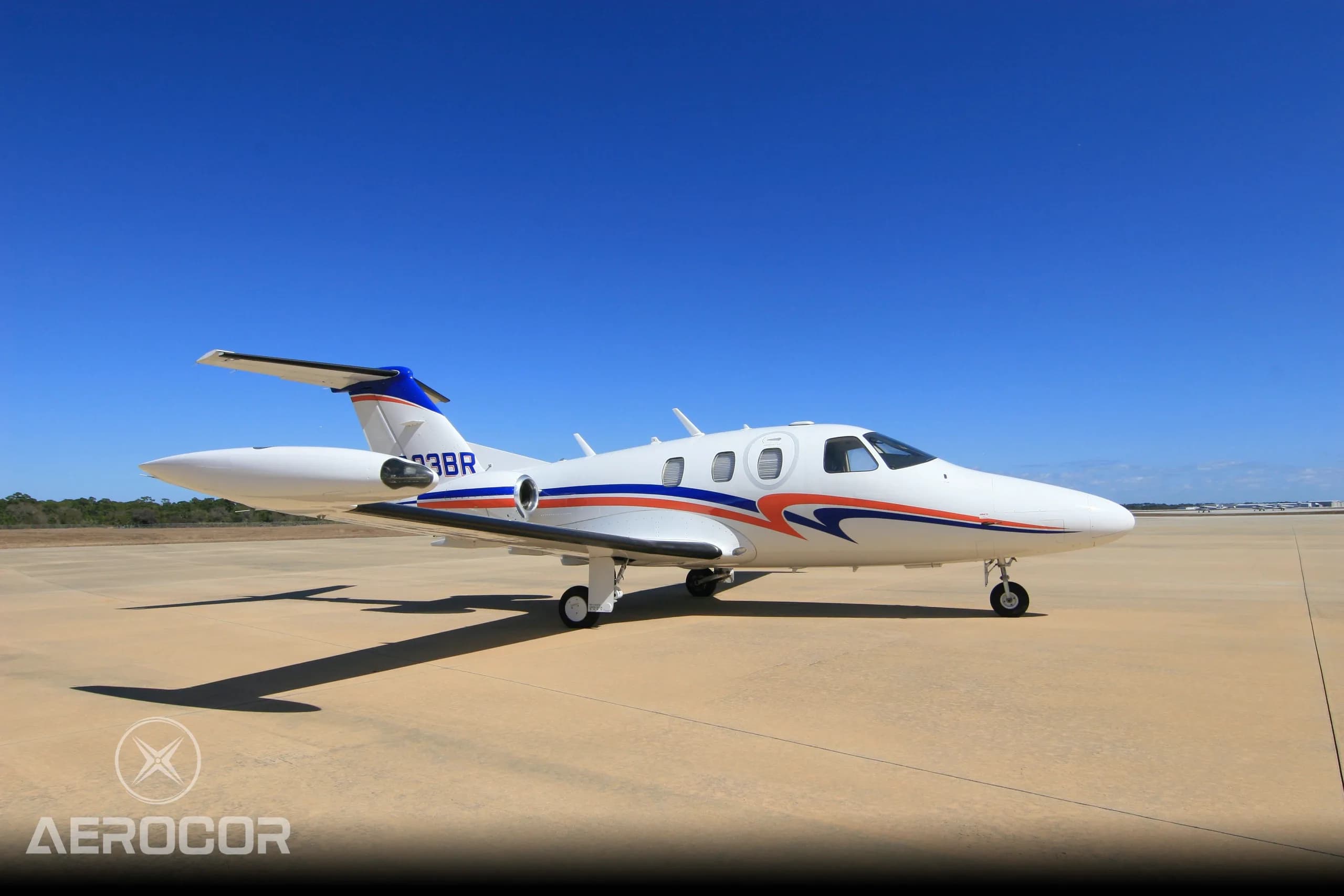 A side view of a white Eclipse 500 jet with blue and orange stripes, tail number N703BR, parked on an airfield.