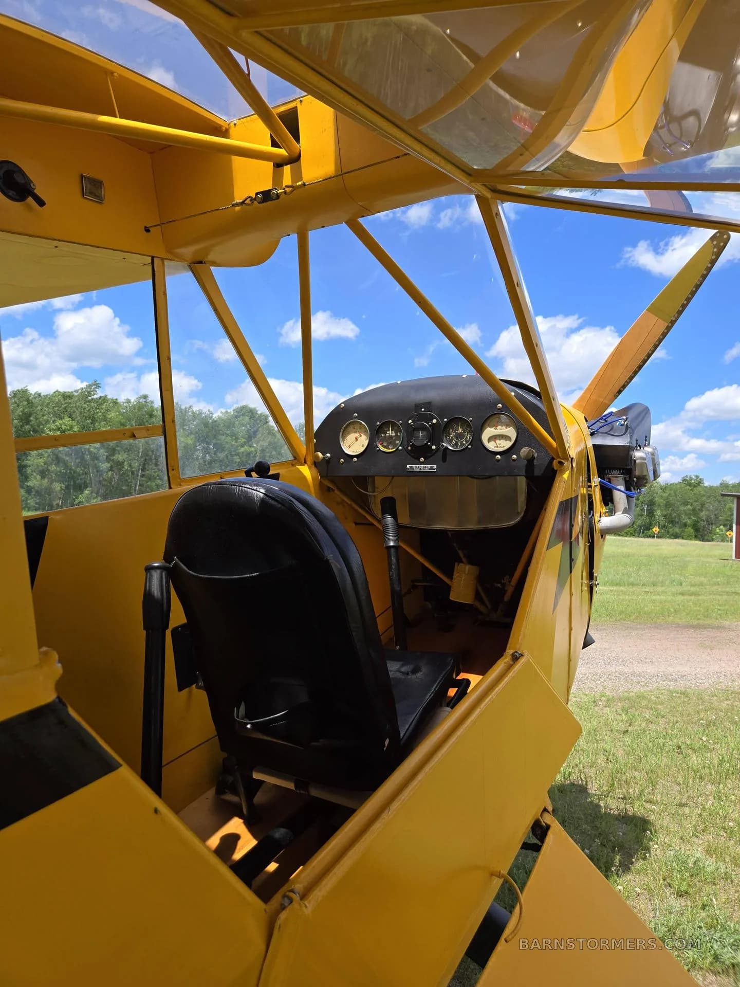 An angled view into the cockpit of a yellow aircraft, showing a black seat and the instrument panel.