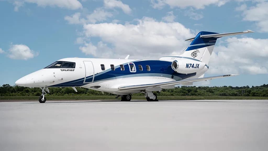 A Pilatus PC-24 business jet, registration N74JX, parked on an airfield under a partly cloudy sky.