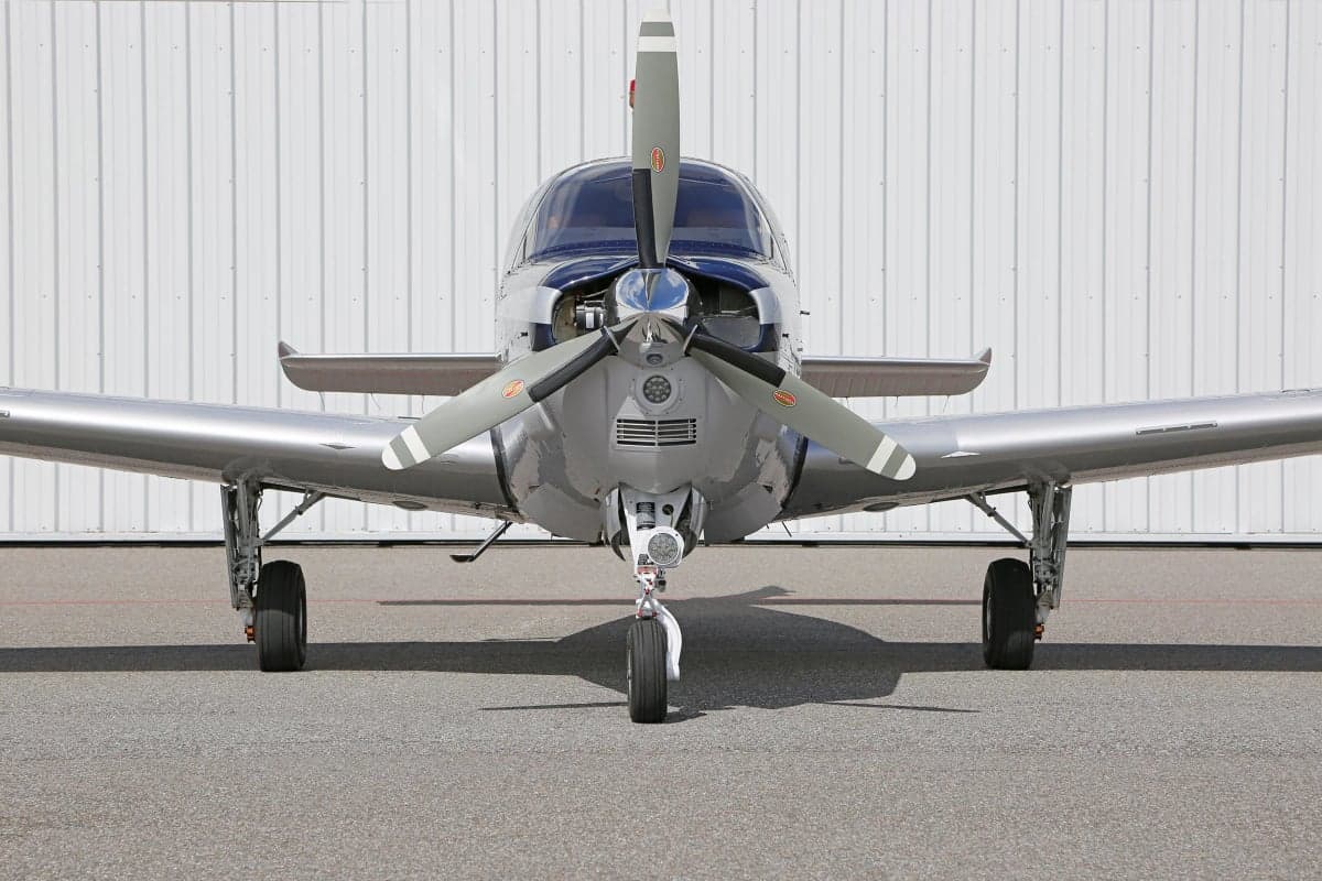 Close-up front view of a Beechcraft Bonanza aircraft parked on the tarmac in front of a hangar.