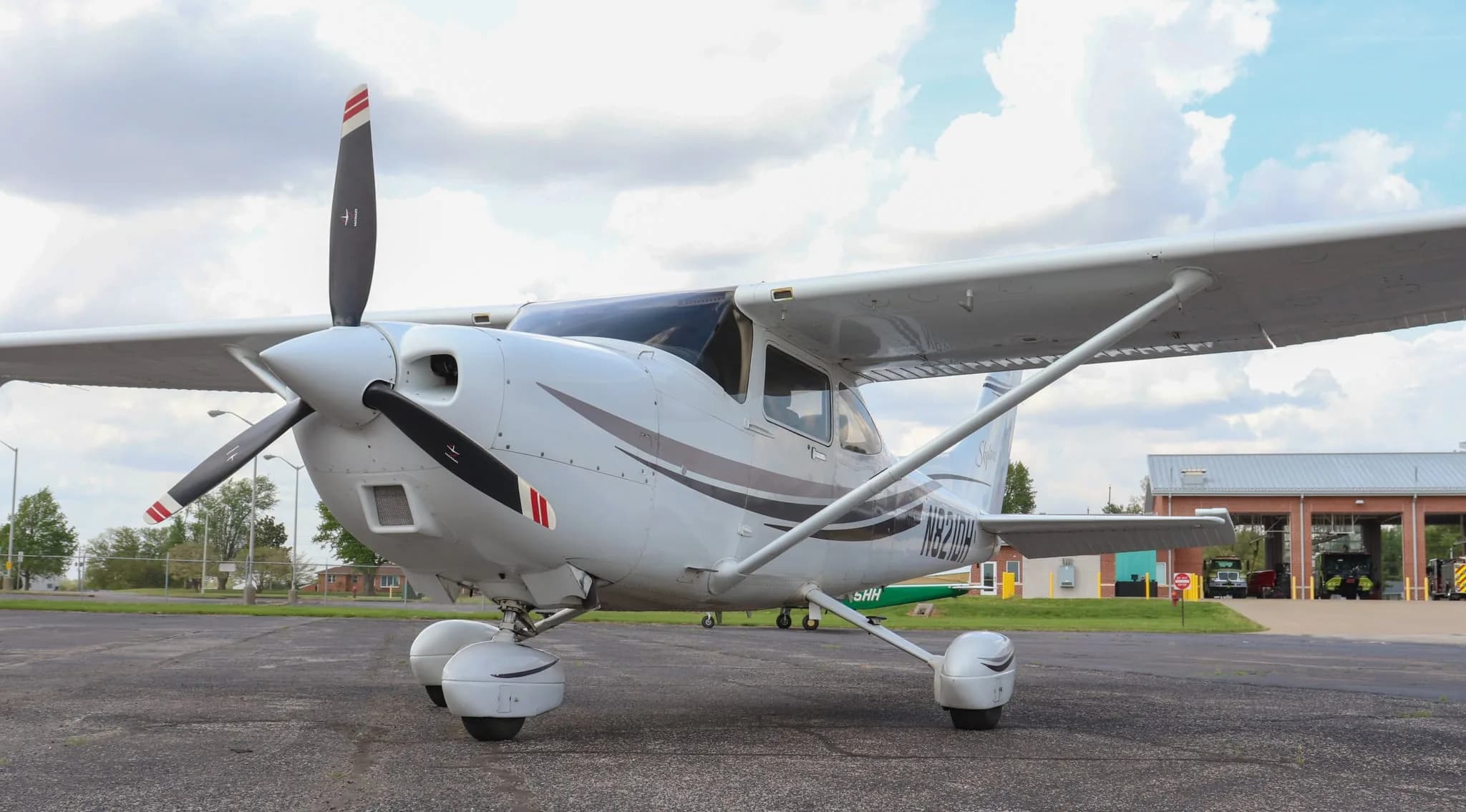 A front-left view of the white Cessna Skylane N821DH with a propeller, parked on an asphalt tarmac.