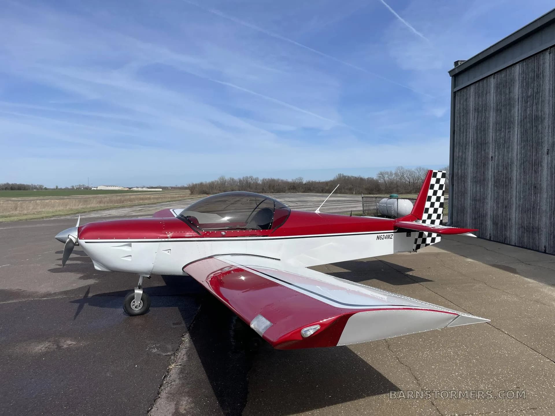 A red and white single-engine aircraft with a checkered tail (N624MZ) is parked on an apron with a runway visible in the background.
