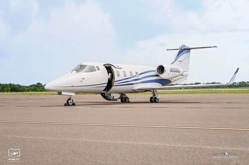 A white business jet with blue stripes, tail number N558RJ, with its main cabin door open, parked on an airfield.