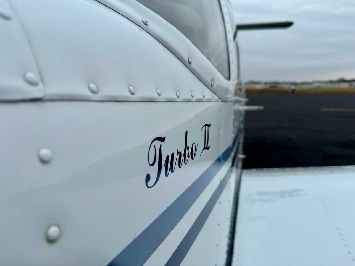 Close-up of the aircraft fuselage showing 'Turbo II' in blue script and blue accent stripes.