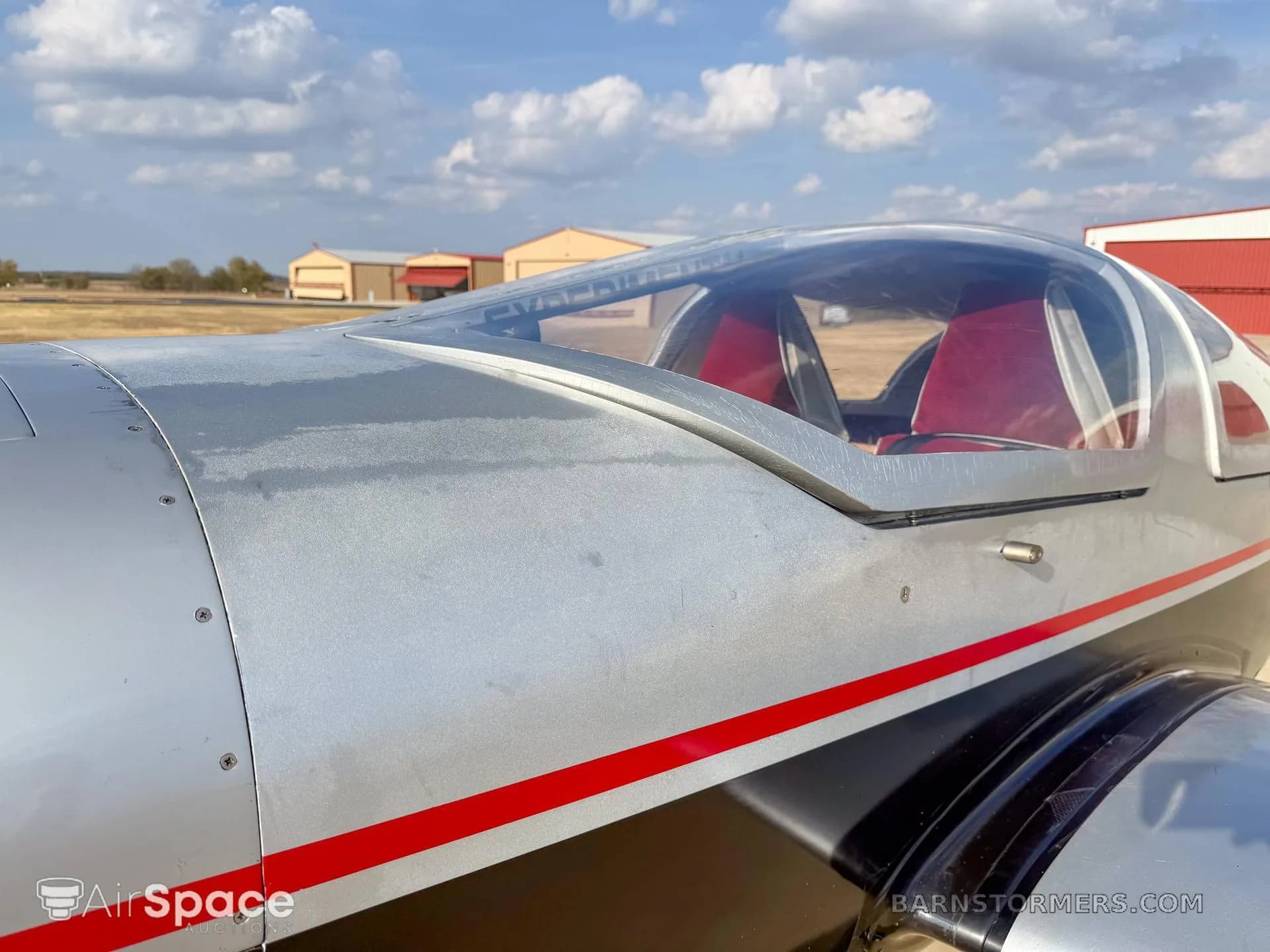 A close-up view of the silver and black fuselage and clear canopy of a small aircraft, showing red interior seats.