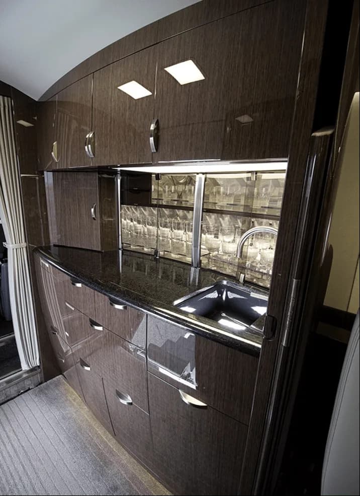 A luxurious aircraft galley with dark wood cabinetry, a black countertop, a sink, and glassware storage.