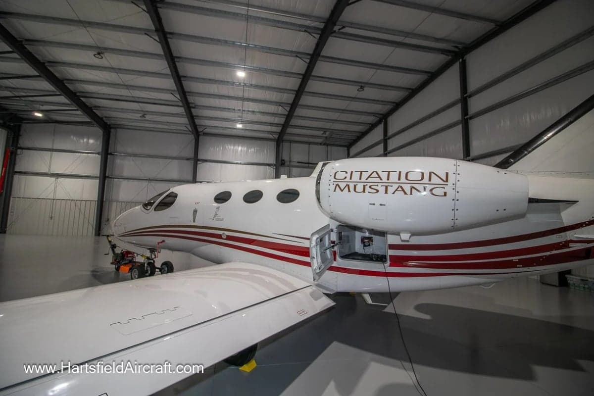 A Cessna Citation Mustang with a white and red paint scheme is parked in a hangar.