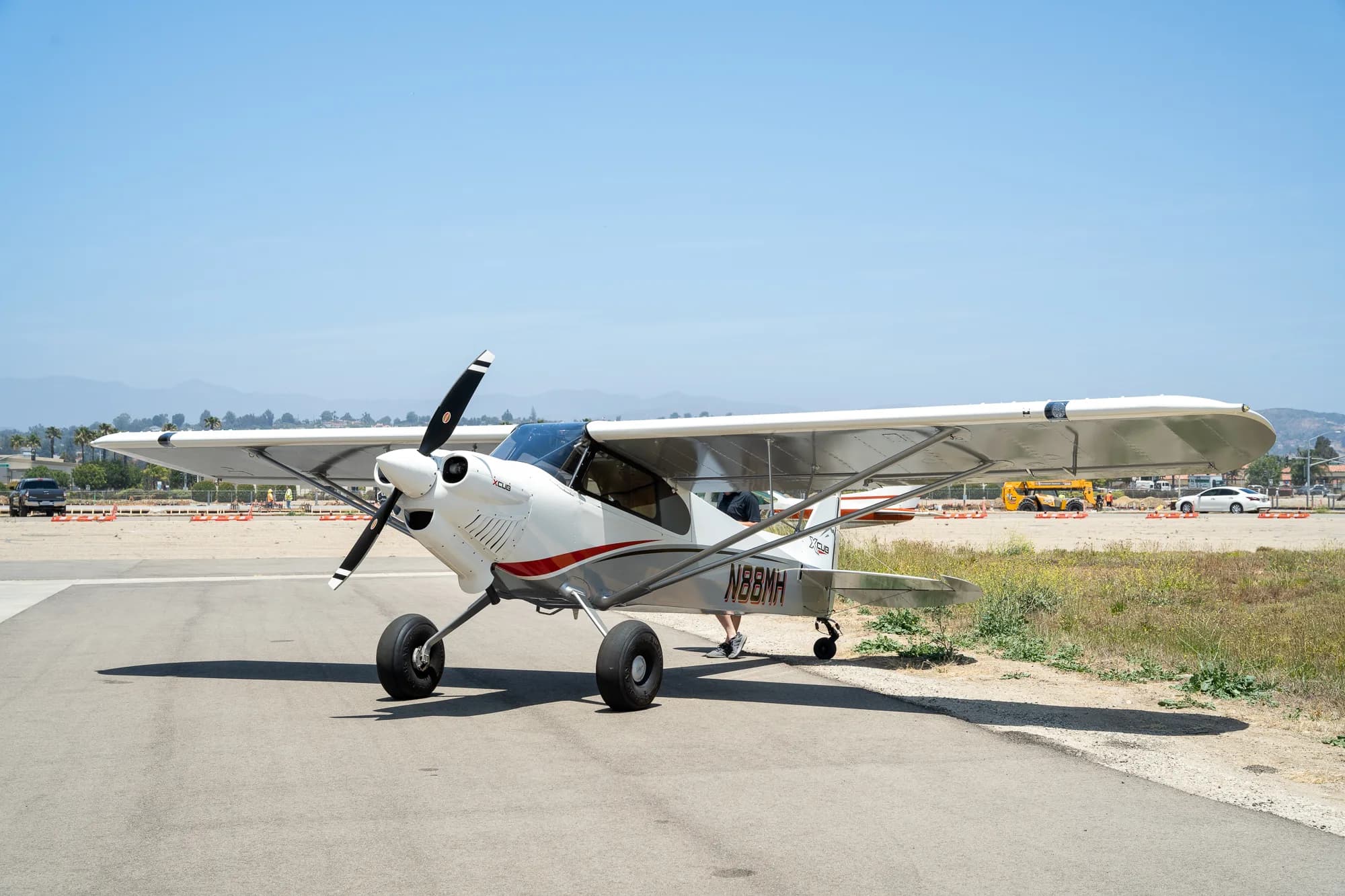 A white and gray CubCrafters XCub, registration N88MH, sits on the tarmac on a sunny day.