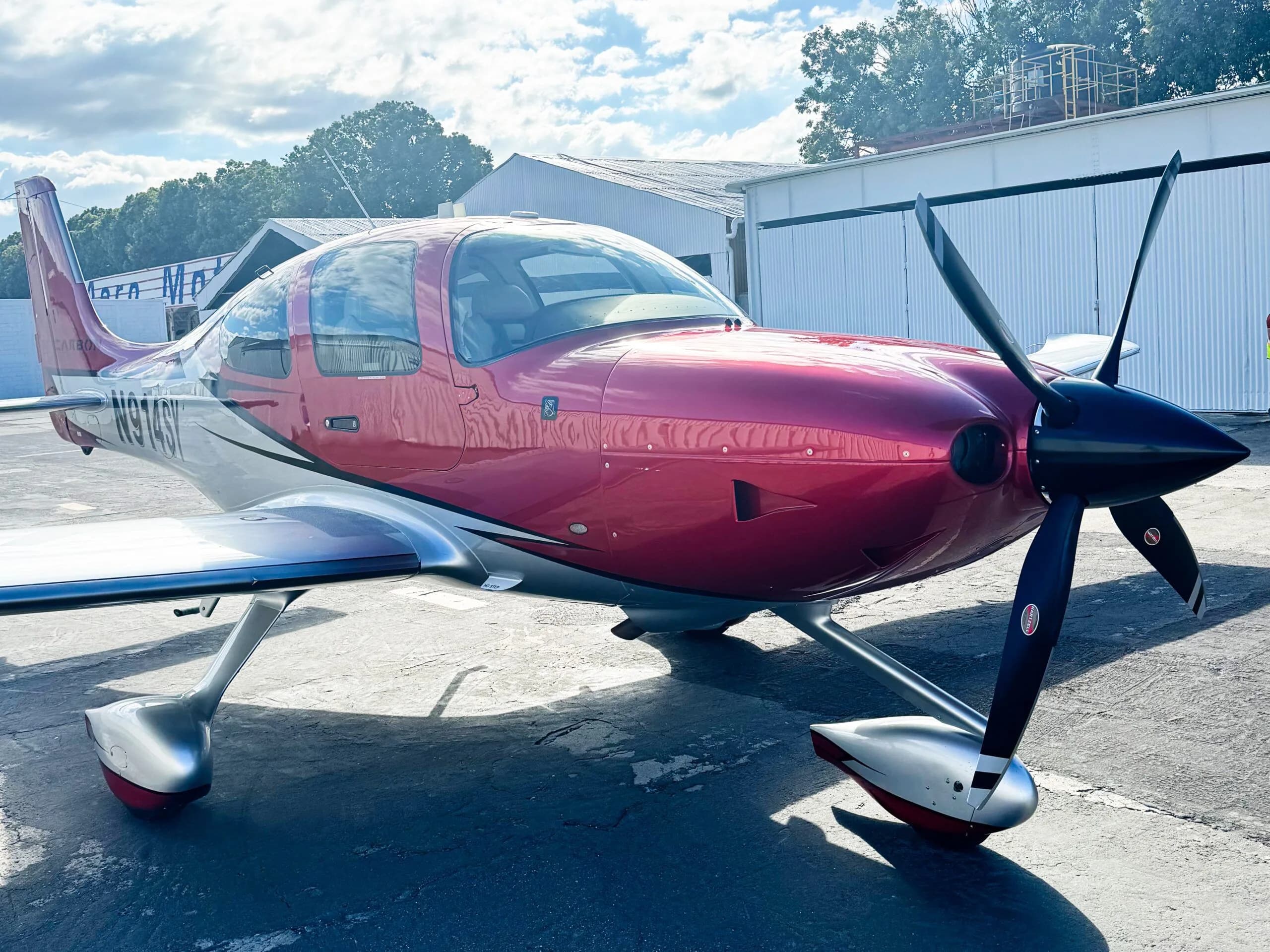 A front-quarter view of the red and silver Cirrus SR22 aircraft N914SY, highlighting its propeller and sleek design.