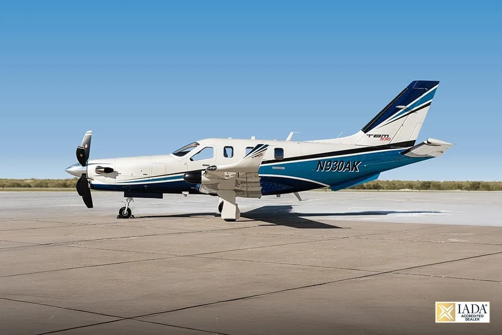 A TBM 930 aircraft with registration N930AK in white and blue livery parked on an airfield.