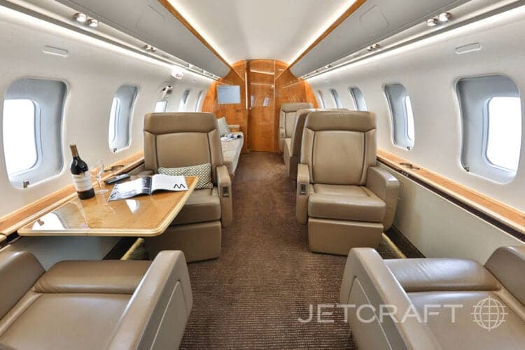 View of the aircraft cabin with leather seats and a table with a bottle of wine.