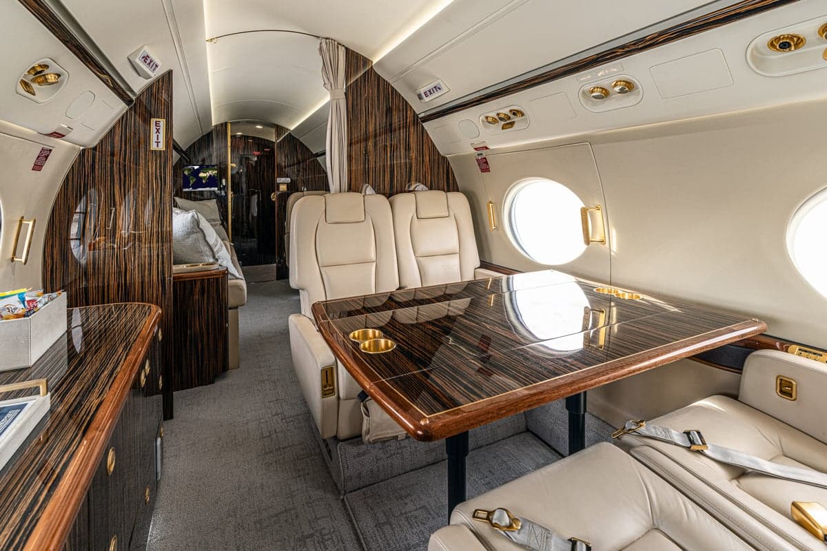 The interior of the aircraft features a table with cup holders and cream-colored leather seats.