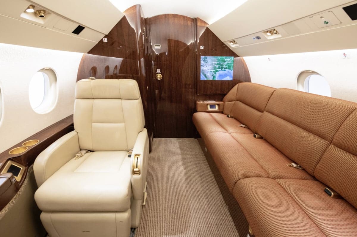 Interior view of the aircraft cabin with a beige leather seat and a brown couch.